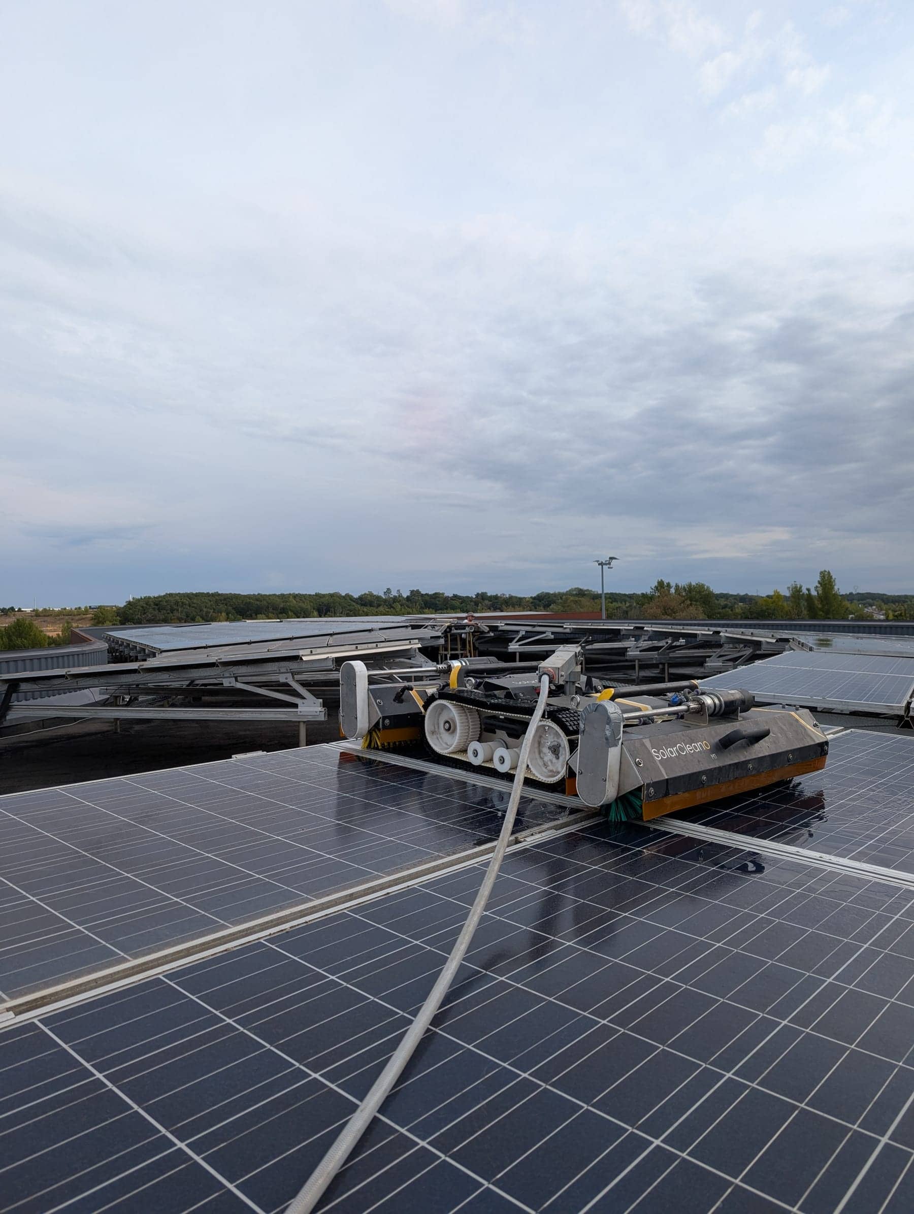 Robot SolarCleano alimenté par un tuyau sur une grande toiture photovoltaïque, campagne à l'horizon