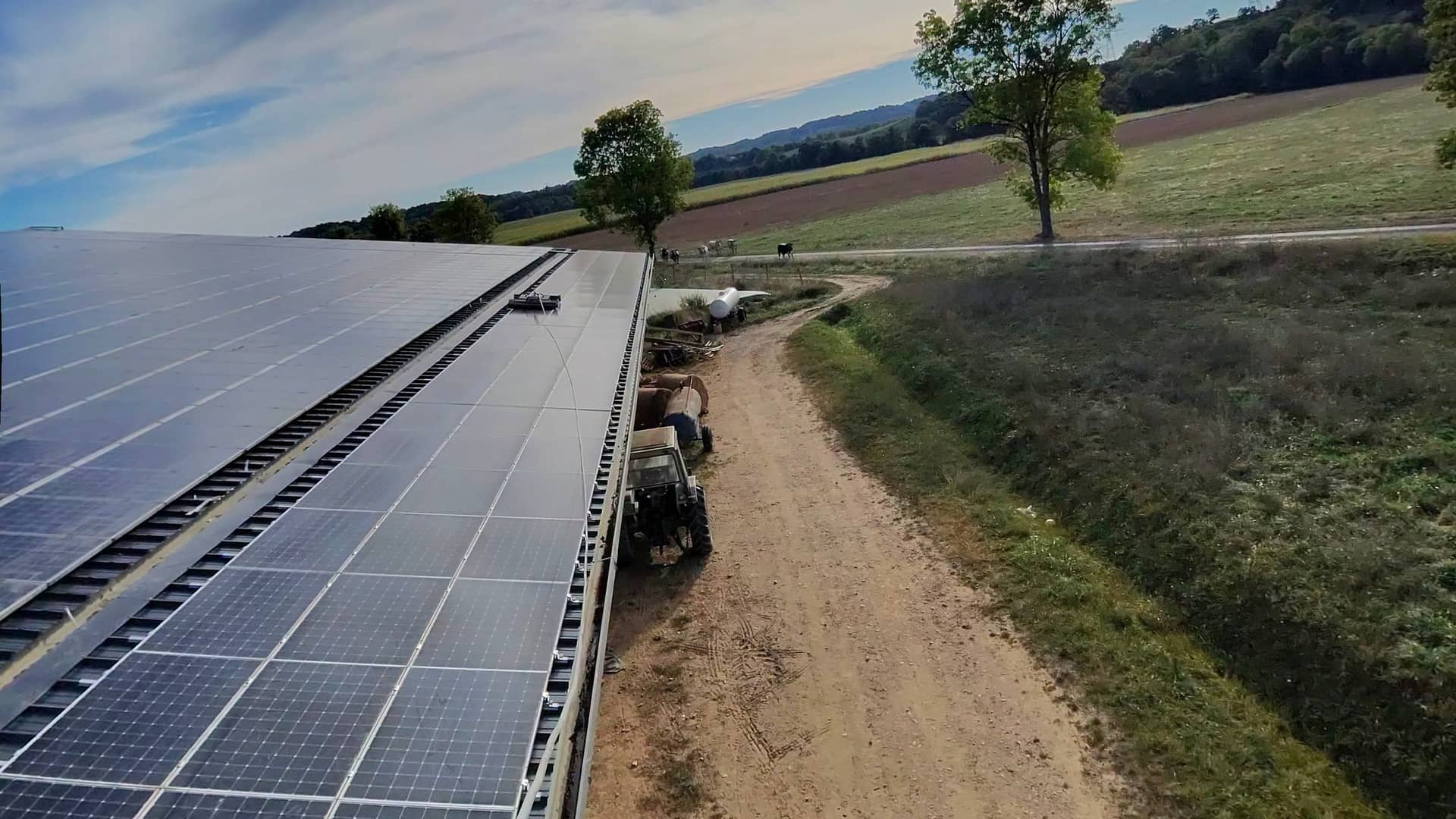Vue depuis une nacelle le long d'une longue rangée de panneaux solaires, chemin rural et soleil rasant