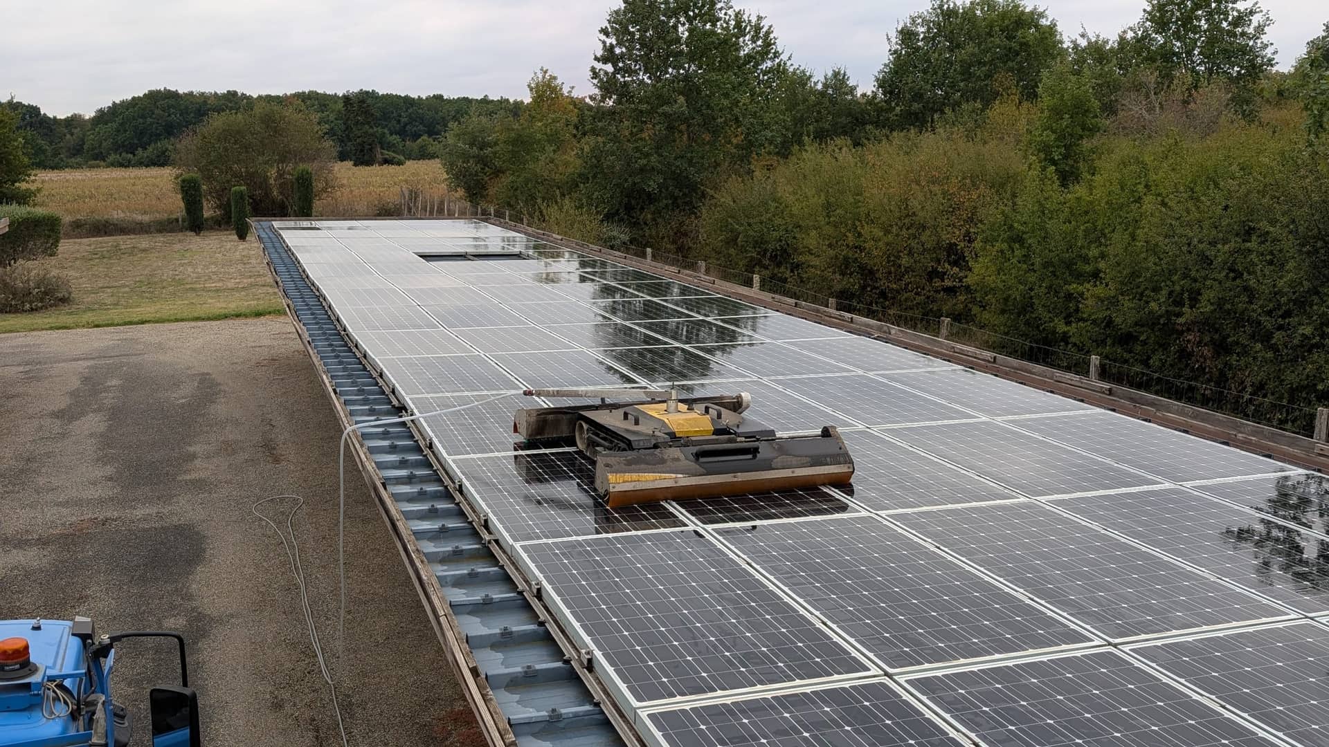Long hangar couvert de panneaux photovoltaïques, robot de nettoyage sur la toiture et camion nacelle au premier plan