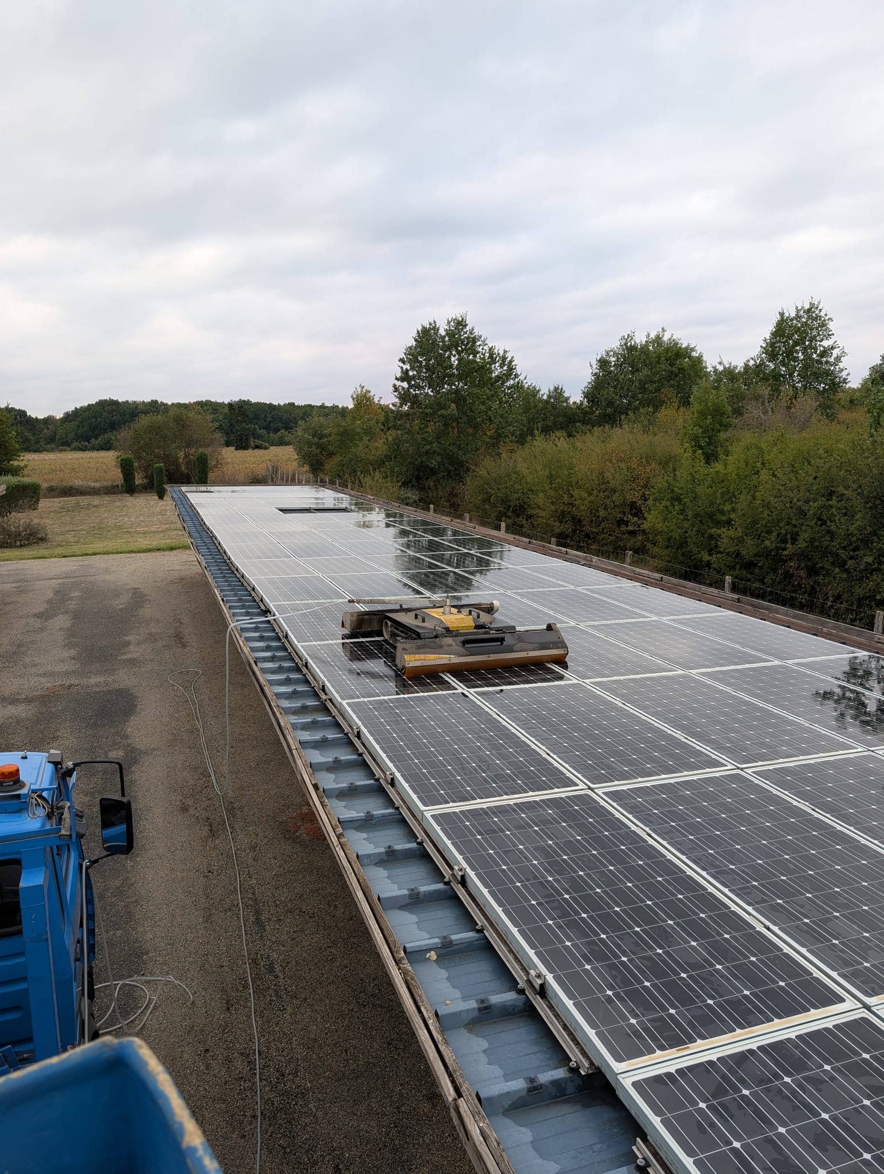 Long hangar couvert de panneaux photovoltaïques, robot de nettoyage sur la toiture et camion nacelle au premier plan