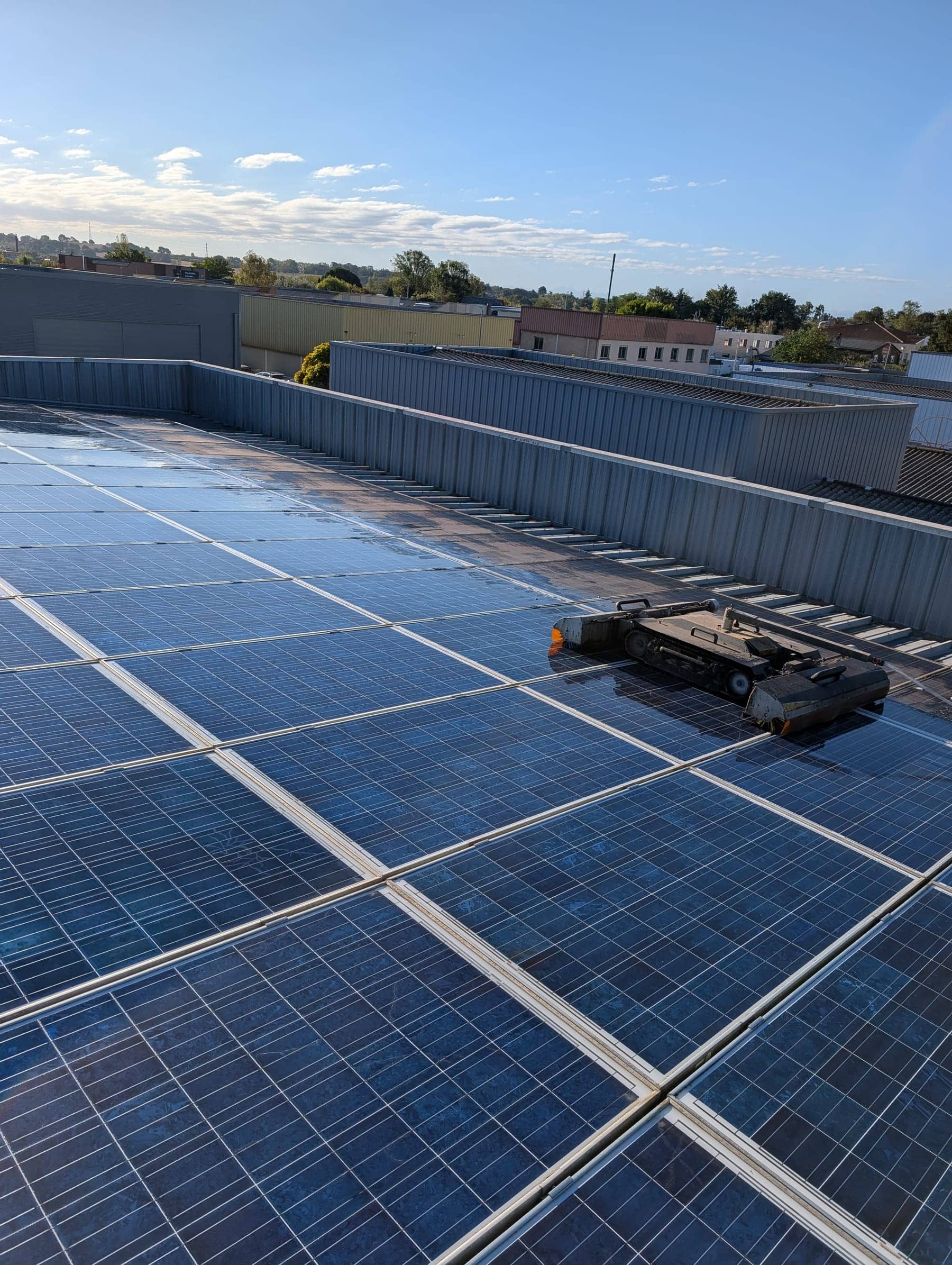 Robot de nettoyage sur une toiture industrielle couverte de panneaux photovoltaïques, ciel bleu