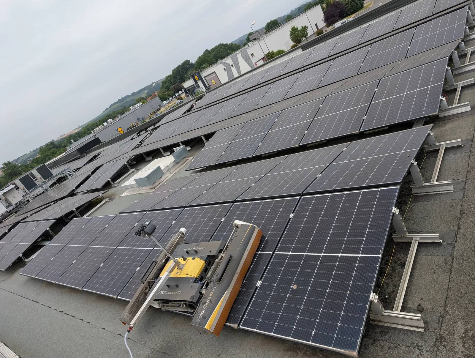 Robot SolarCleano F1 sur des rangées de panneaux inclinés, montées sur des supports au-dessus d'un toit plat