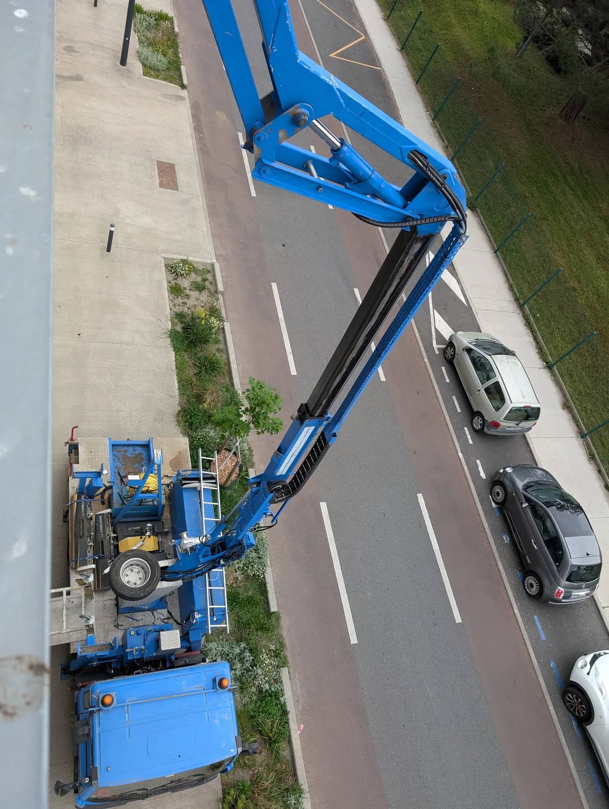 Nacelle bleue au bras levé, vue de haut au-dessus d'une route et de voitures garées