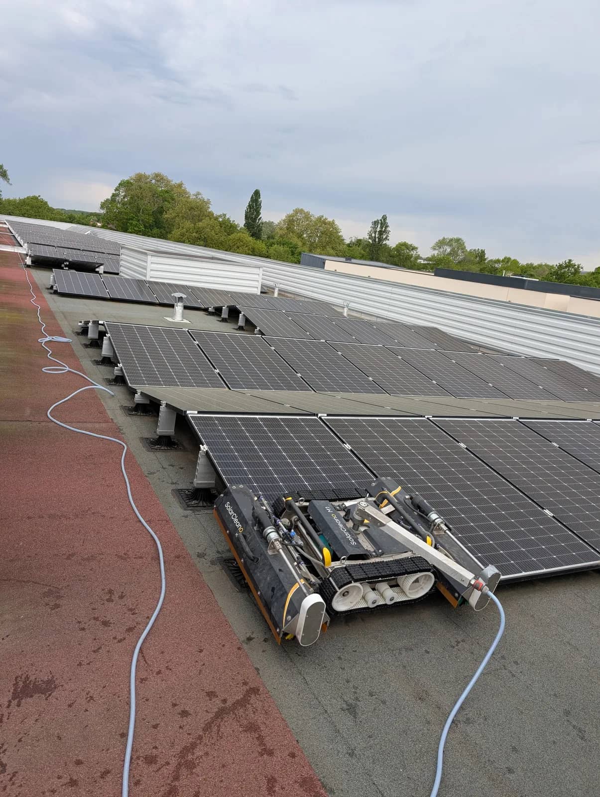 Robot SolarCleano à chenilles, relié à un tuyau, sur une toiture couverte de panneaux
