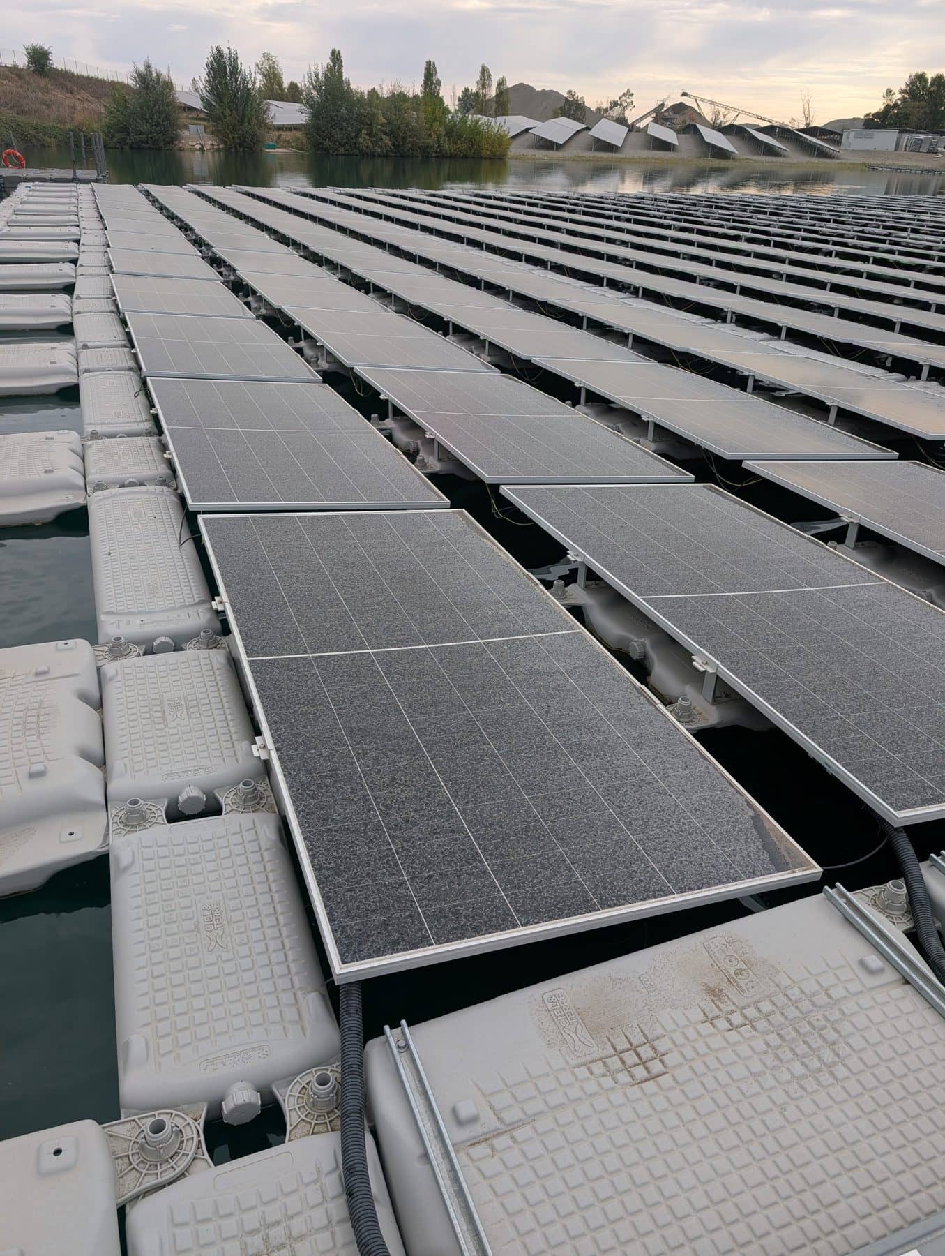 Modules photovoltaïques posés sur des flotteurs, en bord de plan d'eau, certains encore ternis par la poussière